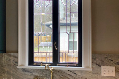 Inspiration for a mid-sized french country galley enclosed kitchen remodel in Other with an undermount sink, shaker cabinets, green cabinets, quartzite countertops, gray backsplash, stone slab backsplash, black appliances, an island and gray countertops