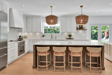 Open concept kitchen - large coastal l-shaped medium tone wood floor and brown floor open concept kitchen idea in Miami with an undermount sink, shaker cabinets, white cabinets, quartz countertops, white backsplash, quartz backsplash, stainless steel appliances, an island and white countertops