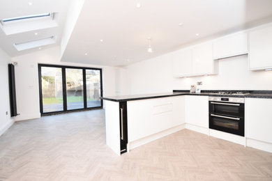 Photo of a large contemporary galley kitchen/diner in London with glass-front cabinets, white cabinets, white splashback, black appliances, vinyl flooring, beige floors and black worktops.