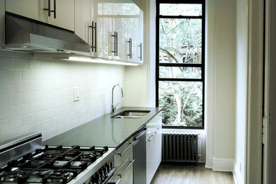 Enclosed kitchen - small contemporary single-wall light wood floor enclosed kitchen idea in New York with a double-bowl sink, white backsplash, stainless steel appliances, no island, flat-panel cabinets, white cabinets, solid surface countertops and ceramic backsplash