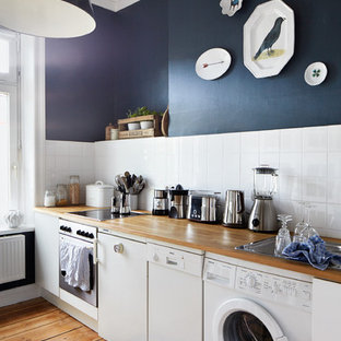 Mid-sized scandinavian kitchen pictures - Inspiration for a mid-sized scandinavian single-wall medium tone wood floor and brown floor kitchen remodel in Munich with a drop-in sink, flat-panel cabinets, white cabinets, white backsplash, white appliances, wood countertops and subway tile backsplash