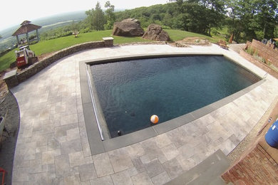 Photo of a large traditional backyard custom-shaped pool in New York with natural stone pavers and a water feature.