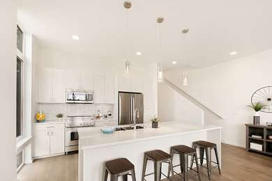 Mid-sized transitional single-wall medium tone wood floor and brown floor eat-in kitchen photo in Seattle with an undermount sink, flat-panel cabinets, light wood cabinets, quartz countertops, white backsplash, ceramic backsplash, stainless steel appliances, an island and white countertops