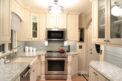 Inspiration for a mid-sized timeless galley light wood floor enclosed kitchen remodel in Other with a farmhouse sink, raised-panel cabinets, white cabinets, quartz countertops, gray backsplash, glass tile backsplash, stainless steel appliances and no island
