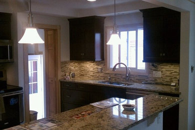 Inspiration for a kitchen remodel in Detroit with an undermount sink, recessed-panel cabinets, dark wood cabinets, granite countertops, glass tile backsplash, stainless steel appliances and a peninsula