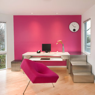 This is an example of a modern home office and library in DC Metro with pink walls, a freestanding desk, light hardwood flooring and beige floors.