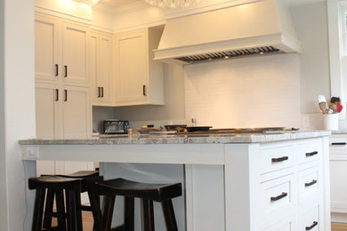 Example of a large transitional u-shaped medium tone wood floor enclosed kitchen design in Seattle with an undermount sink, raised-panel cabinets, white cabinets, granite countertops, white backsplash, ceramic backsplash, stainless steel appliances and an island
