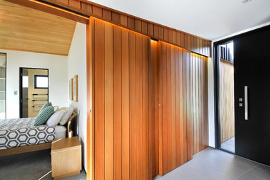 This is an example of a small contemporary entry hall in Auckland with brown walls, porcelain floors, a single front door and a black front door.
