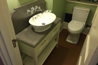 Modelo de cuarto de baño tradicional pequeño con lavabo sobreencimera, armarios con paneles empotrados, puertas de armario blancas, encimera de cemento, sanitario de dos piezas, paredes verdes y suelo de linóleo