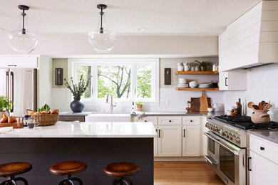 Design ideas for a mid-sized beach style l-shaped eat-in kitchen in Minneapolis with a farmhouse sink, shaker cabinets, white cabinets, quartz benchtops, white splashback, ceramic splashback, stainless steel appliances, medium hardwood floors, with island and white benchtop.
