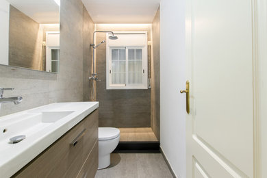 Photo of a mid-sized modern 3/4 bathroom in Barcelona with flat-panel cabinets, dark wood cabinets, an open shower, a one-piece toilet, gray tile, porcelain tile, grey walls, porcelain floors, an integrated sink, marble benchtops, grey floor, a shower curtain and white benchtops.