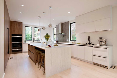 Mid-sized trendy light wood floor kitchen photo in Boston with a double-bowl sink, flat-panel cabinets, white cabinets, quartzite countertops, gray backsplash, porcelain backsplash, black appliances, an island and white countertops