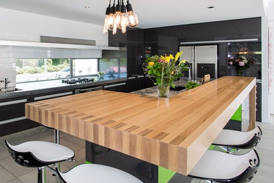 This is an example of a mid-sized contemporary l-shaped eat-in kitchen in Christchurch with an undermount sink, beaded inset cabinets, black cabinets, wood benchtops, window splashback, stainless steel appliances, ceramic floors and with island.