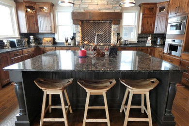 Inspiration for a rustic kitchen remodel in Grand Rapids with a farmhouse sink, recessed-panel cabinets, dark wood cabinets, quartz countertops, black backsplash, travertine backsplash, stainless steel appliances, an island and brown countertops