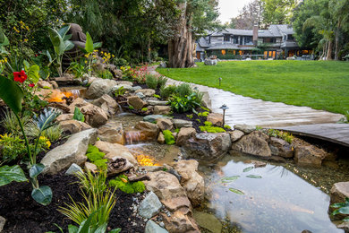 This is an example of a mid-sized contemporary backyard partial sun formal garden for spring in Los Angeles with with pond and natural stone pavers.