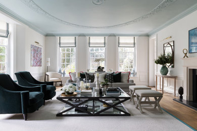 This is an example of a large classic formal enclosed living room in Surrey with white walls, medium hardwood flooring, a standard fireplace, a stone fireplace surround, a wall mounted tv, brown floors, panelled walls and a dado rail.