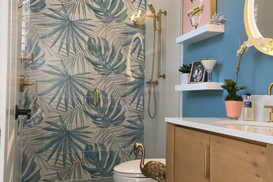 Small beach style multicolored tile and porcelain tile mosaic tile floor, green floor and single-sink walk-in shower photo in Orlando with flat-panel cabinets, light wood cabinets, a one-piece toilet, blue walls, an undermount sink, quartzite countertops, a hinged shower door, white countertops and a freestanding vanity