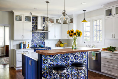 Ejemplo de cocina tradicional renovada de tamaño medio con puertas de armario blancas, salpicadero azul, electrodomésticos de acero inoxidable, suelo de madera en tonos medios, una isla y encimeras blancas