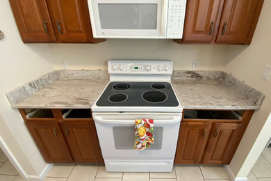 Example of a mid-sized trendy l-shaped ceramic tile and white floor enclosed kitchen design in Bridgeport with an undermount sink, medium tone wood cabinets, granite countertops, granite backsplash, white appliances, no island and white countertops