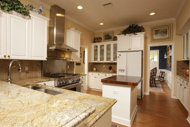Example of a mid-sized cottage l-shaped light wood floor eat-in kitchen design in Jacksonville with a double-bowl sink, raised-panel cabinets, white cabinets, soapstone countertops, beige backsplash, ceramic backsplash, white appliances and an island