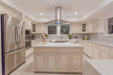 Huge elegant u-shaped travertine floor and gray floor enclosed kitchen photo in Los Angeles with an undermount sink, raised-panel cabinets, beige cabinets, quartz countertops, gray backsplash, marble backsplash, stainless steel appliances and an island