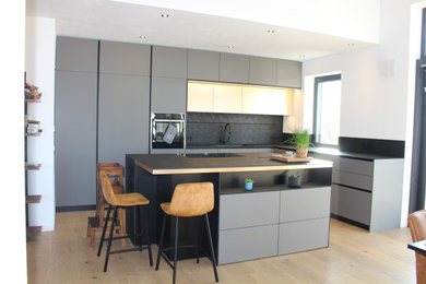 Große Moderne Küche in L-Form mit Unterbauwaschbecken, grauen Schränken, Laminat-Arbeitsplatte, Küchenrückwand in Schwarz, gebeiztem Holzboden, Kücheninsel und schwarzer Arbeitsplatte in München