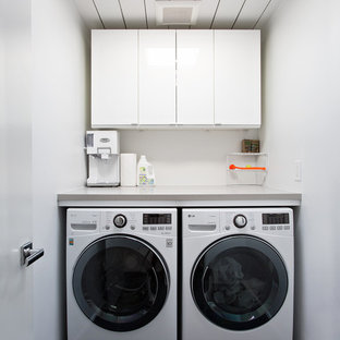 This is an example of a small midcentury single-wall separated utility room in San Francisco with flat-panel cabinets, white cabinets, white walls, a side by side washer and dryer, black floors and grey worktops.