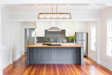 Example of a mid-sized transitional galley medium tone wood floor and multicolored floor eat-in kitchen design in Austin with an undermount sink, shaker cabinets, white cabinets, wood countertops, gray backsplash, brick backsplash, stainless steel appliances and an island