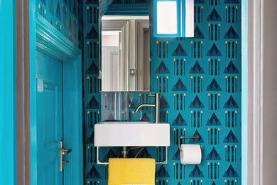 This is an example of a medium sized bohemian cloakroom in London with a wall mounted toilet, blue walls, mosaic tile flooring, multi-coloured floors, a feature wall, a wallpapered ceiling and wallpapered walls.