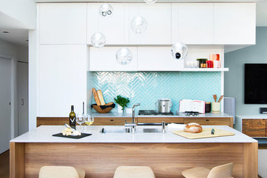 Inspiration for a mid-sized contemporary galley open plan kitchen in Vancouver with a double-bowl sink, flat-panel cabinets, white cabinets, blue splashback, with island, quartz benchtops, glass tile splashback, panelled appliances and medium hardwood floors.