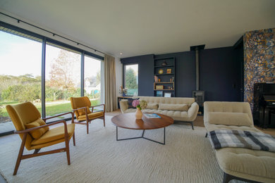 Cette image montre un grand salon beige et blanc design ouvert avec une bibliothèque ou un coin lecture, un mur bleu, parquet clair, un poêle à bois, un téléviseur dissimulé, du papier peint et un escalier.