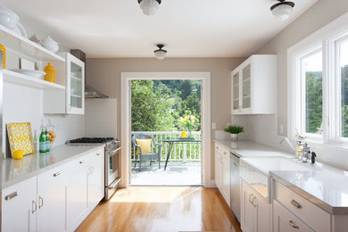 Mid-sized contemporary galley eat-in kitchen in San Francisco with a farmhouse sink, shaker cabinets, white cabinets, quartzite benchtops, white splashback, subway tile splashback, stainless steel appliances, medium hardwood floors, no island and brown floor.