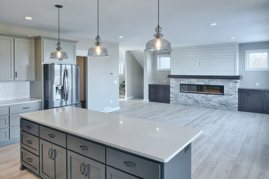 Photo of a large traditional l-shaped open plan kitchen in Other with a farmhouse sink, shaker cabinets, grey cabinets, quartz benchtops, white splashback, ceramic splashback, stainless steel appliances, vinyl floors, with island and grey floor.