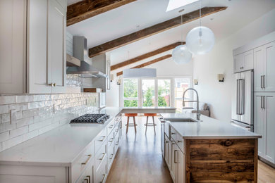 Mid-sized transitional galley medium tone wood floor and exposed beam eat-in kitchen photo in Boston with a farmhouse sink, shaker cabinets, white cabinets, quartz countertops, white backsplash, porcelain backsplash, stainless steel appliances, an island and white countertops