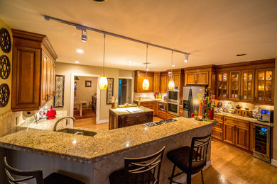 Eat-in kitchen - large traditional galley medium tone wood floor eat-in kitchen idea in Atlanta with an undermount sink, raised-panel cabinets, medium tone wood cabinets, granite countertops, beige backsplash, ceramic backsplash, stainless steel appliances and an island