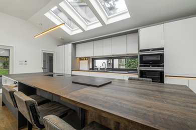 Foto de cocina comedor abovedada contemporánea de tamaño medio con fregadero bajoencimera, armarios con paneles lisos, puertas de armario grises, encimera de granito, electrodomésticos negros, suelo de madera en tonos medios, una isla, suelo marrón y encimeras marrones