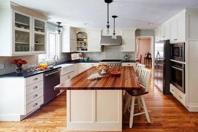 Example of a mid-sized farmhouse u-shaped medium tone wood floor enclosed kitchen design in Chicago with a farmhouse sink, shaker cabinets, white cabinets, granite countertops, white backsplash, subway tile backsplash and stainless steel appliances