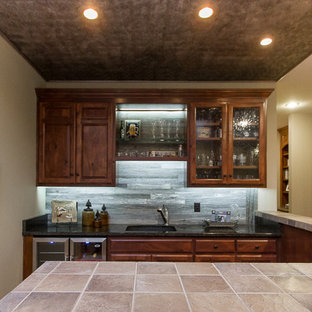 カンザスシティの中サイズのラスティックスタイルのおしゃれな着席型バー (アンダーカウンターシンク、レイズドパネル扉のキャビネット、濃色木目調キャビネット、タイルカウンター、グレーのキッチンパネル、木材のキッチンパネル、無垢フローリング、茶色い床) の写真