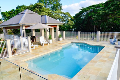 Photo of a large traditional backyard rectangular natural pool in Cairns with a pool house and natural stone pavers.