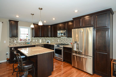 Inspiration for a mid-sized timeless l-shaped medium tone wood floor eat-in kitchen remodel in New York with an undermount sink, raised-panel cabinets, dark wood cabinets, granite countertops, multicolored backsplash, porcelain backsplash, stainless steel appliances and an island
