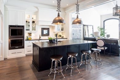 Large trendy galley medium tone wood floor and brown floor open concept kitchen photo in Other with an undermount sink, shaker cabinets, white cabinets, granite countertops, white backsplash, stainless steel appliances and an island