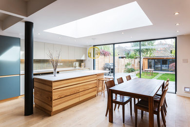 Inspiration for a contemporary single-wall kitchen/diner in London with a submerged sink, flat-panel cabinets, beige cabinets, beige splashback, light hardwood flooring, an island, beige floors and white worktops.