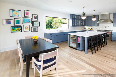 Photo of a scandinavian kitchen/diner in Los Angeles with shaker cabinets, blue cabinets, light hardwood flooring and an island.