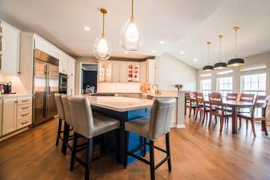 Eat-in kitchen - mid-sized transitional l-shaped medium tone wood floor and brown floor eat-in kitchen idea in Baltimore with a farmhouse sink, shaker cabinets, blue cabinets, quartz countertops, white backsplash, porcelain backsplash, stainless steel appliances, an island and white countertops