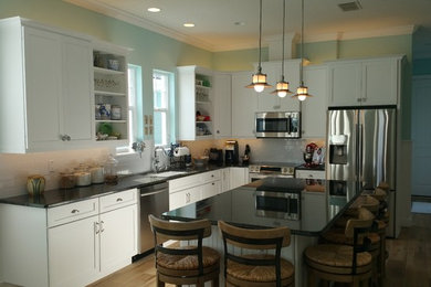 Kitchen - mid-sized coastal l-shaped medium tone wood floor and brown floor kitchen idea in Orlando with an undermount sink, shaker cabinets, white cabinets, granite countertops, beige backsplash, stainless steel appliances and an island