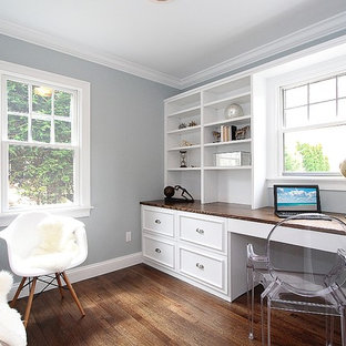 This is an example of a small modern home office and library in New York with grey walls, dark hardwood flooring and a built-in desk.