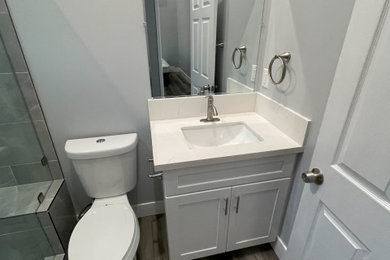 Mid-sized minimalist 3/4 gray tile and ceramic tile vinyl floor, brown floor, single-sink and vaulted ceiling bathroom photo in Los Angeles with shaker cabinets, white cabinets, a two-piece toilet, gray walls, an undermount sink, quartzite countertops, a hinged shower door, beige countertops and a freestanding vanity