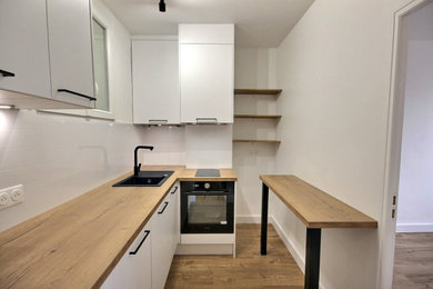 Bild på ett avskilt, litet vintage brun brunt l-kök, med en enkel diskho, släta luckor, vita skåp, laminatbänkskiva, vitt stänkskydd, svarta vitvaror, vinylgolv och brunt golv