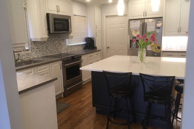 Example of a mid-sized classic u-shaped light wood floor enclosed kitchen design in Toronto with an undermount sink, raised-panel cabinets, white cabinets, quartz countertops, gray backsplash, glass tile backsplash, stainless steel appliances, an island and multicolored countertops