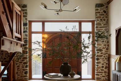 Example of a large cottage medium tone wood floor, brown floor, vaulted ceiling and exposed beam entryway design in Philadelphia with beige walls and a medium wood front door